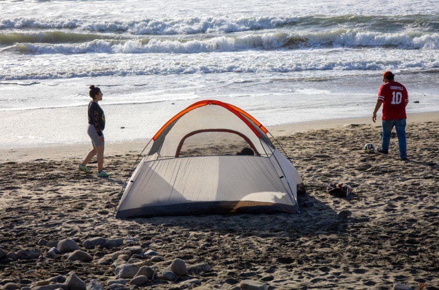 A person standing on the beach near an orange and white tent.